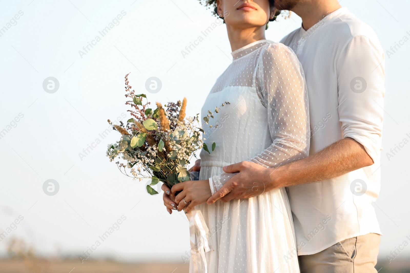 Photo of Happy newlyweds with beautiful field bouquet outdoors, closeup