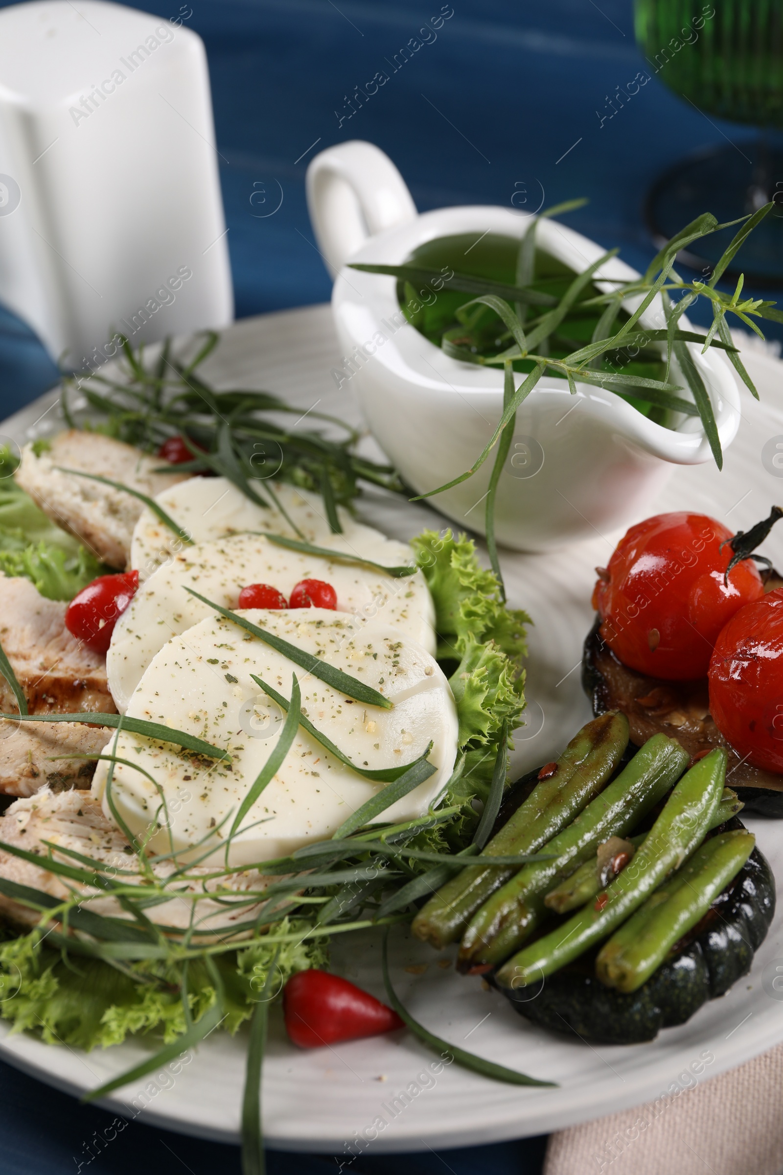 Photo of Tasty mozzarella, chicken and vegetables with tarragon on table, closeup