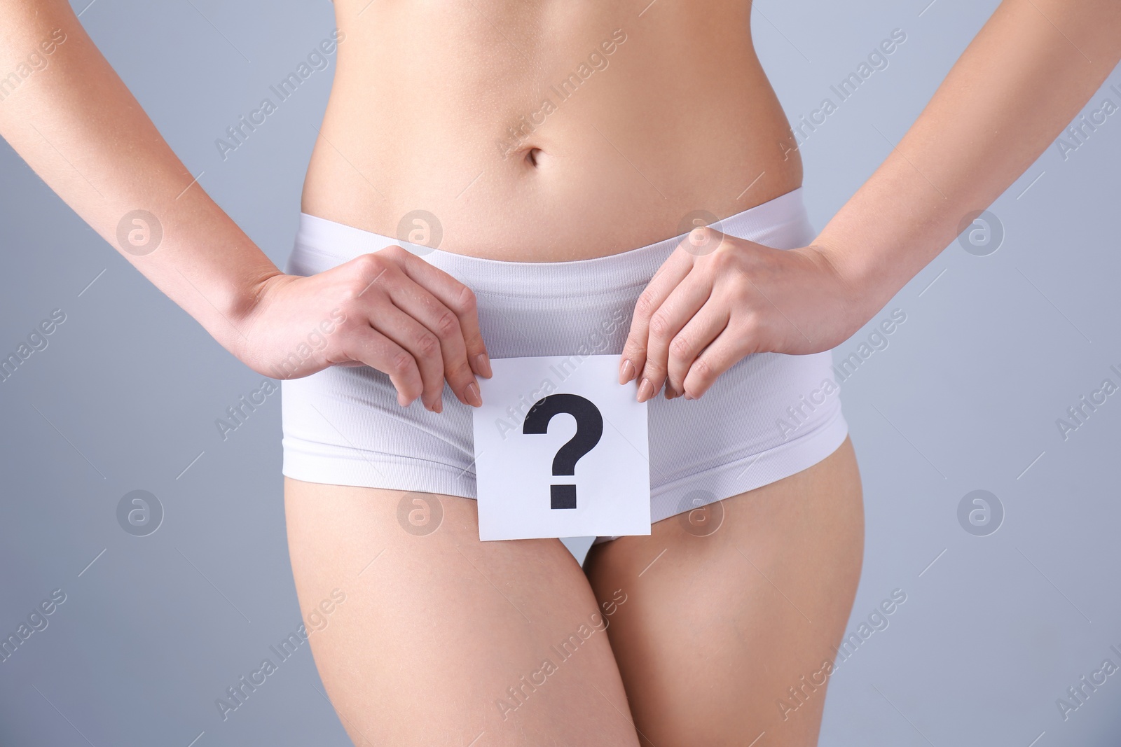 Photo of Young woman holding paper with question mark near underwear on grey background. Gynecology