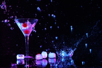 Photo of Martini splashing out of glass near ice on black background