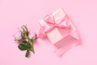 Photo of Gift box and beautiful rose flowers on pink background, flat lay