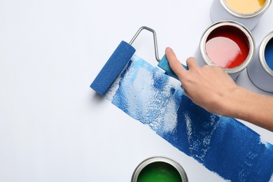 Woman painting with roller brush near cans on white background, closeup view