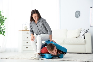 Photo of Young couple having fun while packing suitcase for summer journey at home