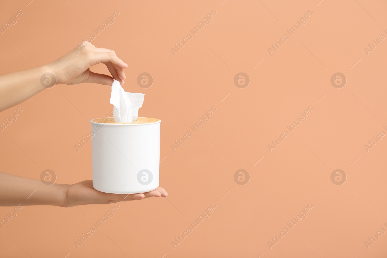 Photo of Woman taking paper tissue from holder on light brown background, closeup. Space for text