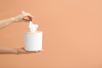 Photo of Woman taking paper tissue from holder on light brown background, closeup. Space for text