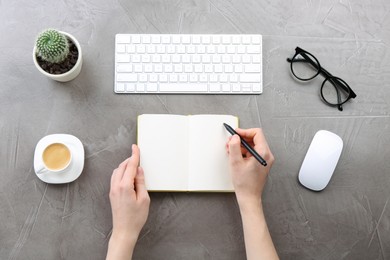 Woman writing in notebook at grey table, top view