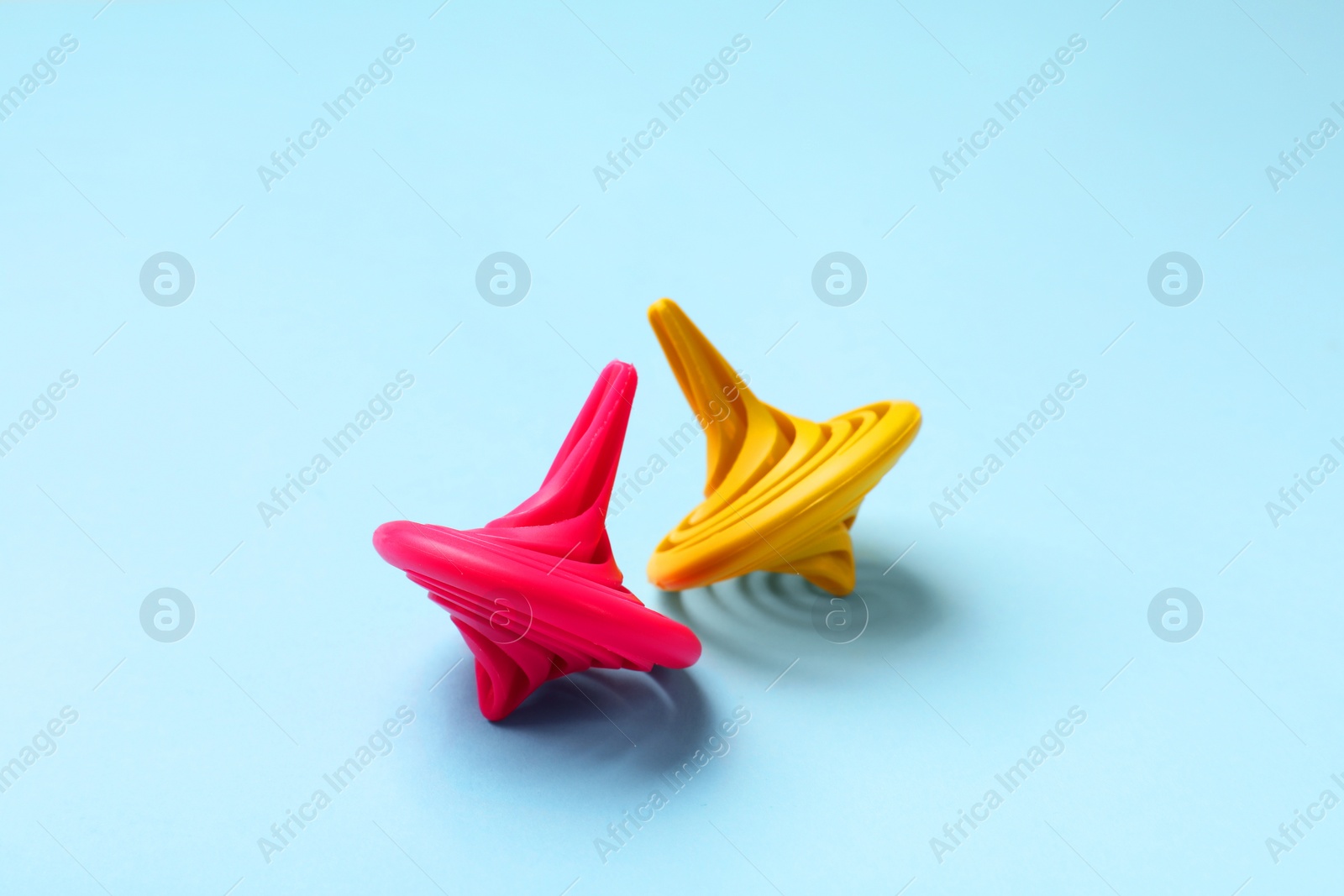 Photo of Yellow and pink spinning tops on light blue background, closeup