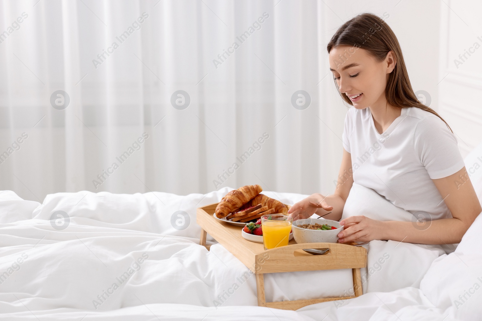 Photo of Smiling woman having breakfast in bed at home. Space for text