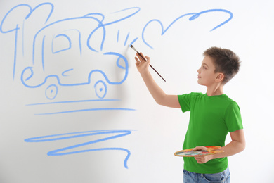 Little child drawing car on white wall indoors