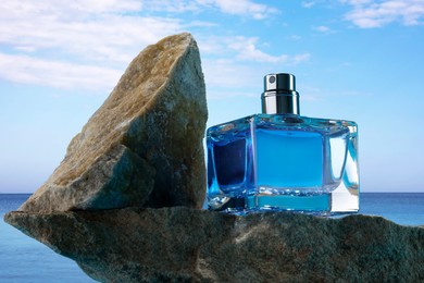 Image of Bottle of aquatic perfume on rock near ocean. Fresh sea breeze scent