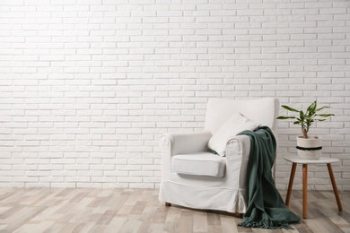 Photo of Comfortable armchair near brick wall in modern room interior. Space for text