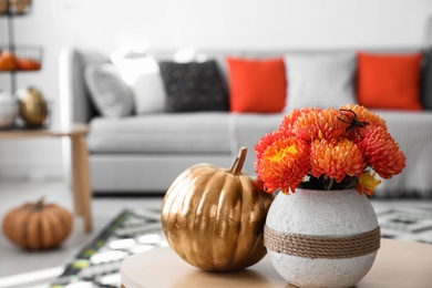 Photo of Beautiful flowers with toy spider and pumpkin on table in room. Halloween interior decor