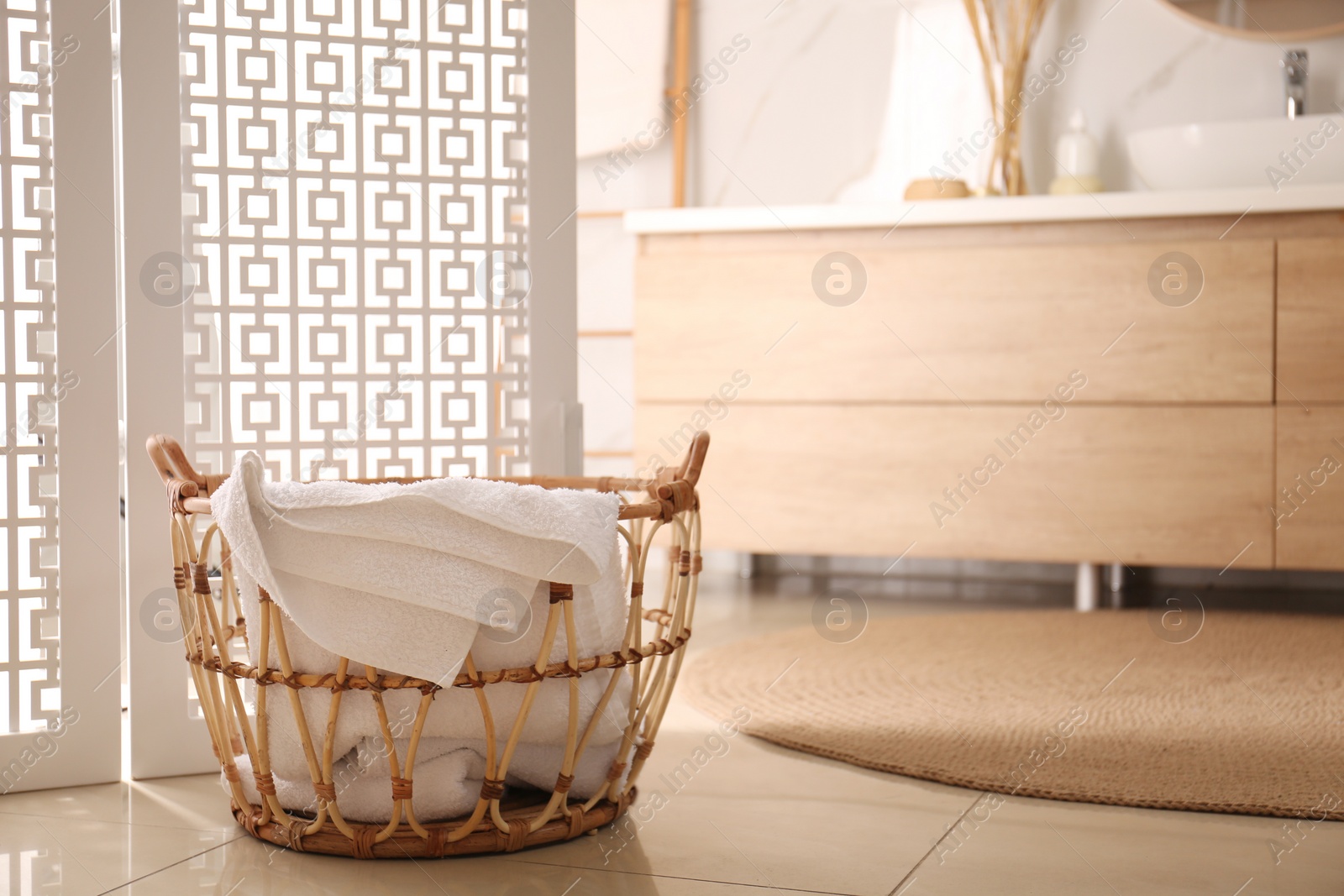 Photo of Basket with clean towel near folding screen in bathroom. Stylish interior design