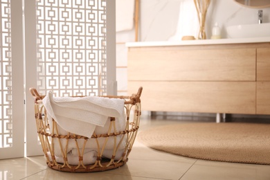 Photo of Basket with clean towel near folding screen in bathroom. Stylish interior design