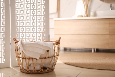 Basket with clean towel near folding screen in bathroom. Stylish interior design