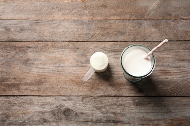 Glass of protein shake, scoop with powder and space for text on wooden background, top view