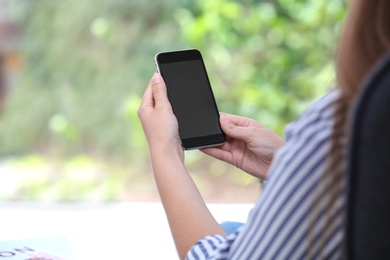 Woman holding smartphone with blank screen on blurred background. Mockup for design