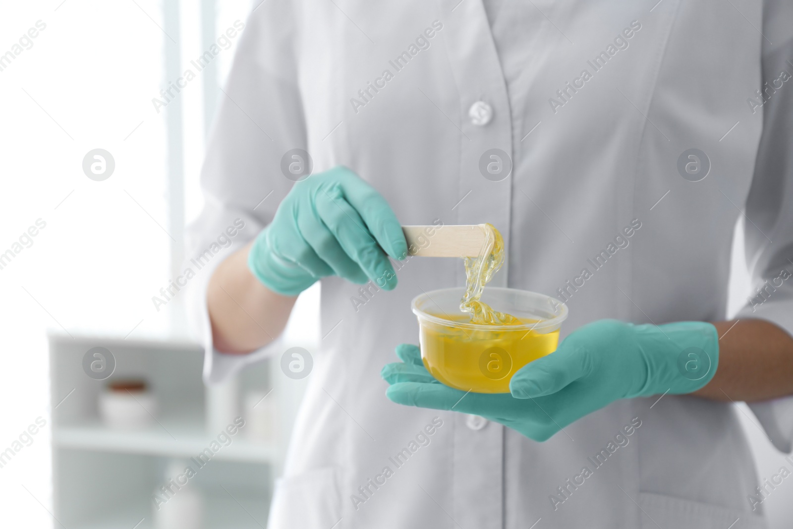 Photo of Beautician with bowl of wax and spatula in salon, closeup. Epilation procedure