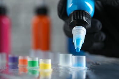 Photo of Tattoo artist dripping blue tattoo ink into cap on table, closeup