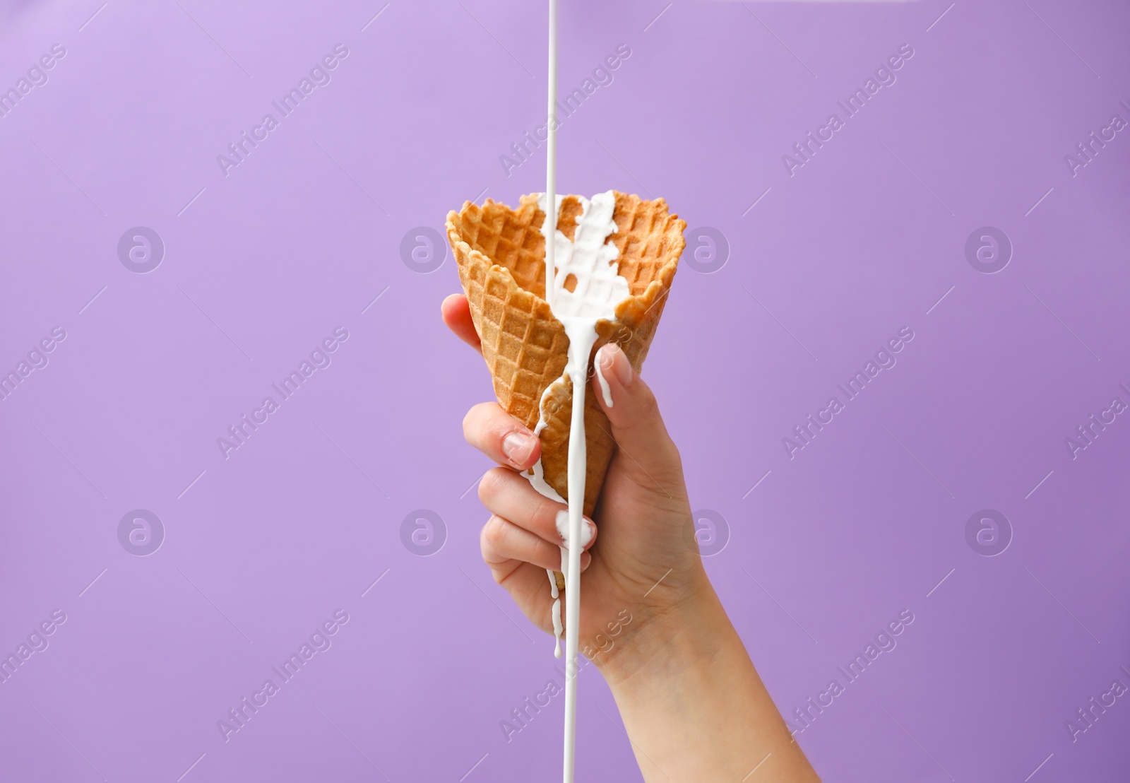 Photo of Pouring molten ice cream into wafer cone held by woman on violet background, closeup