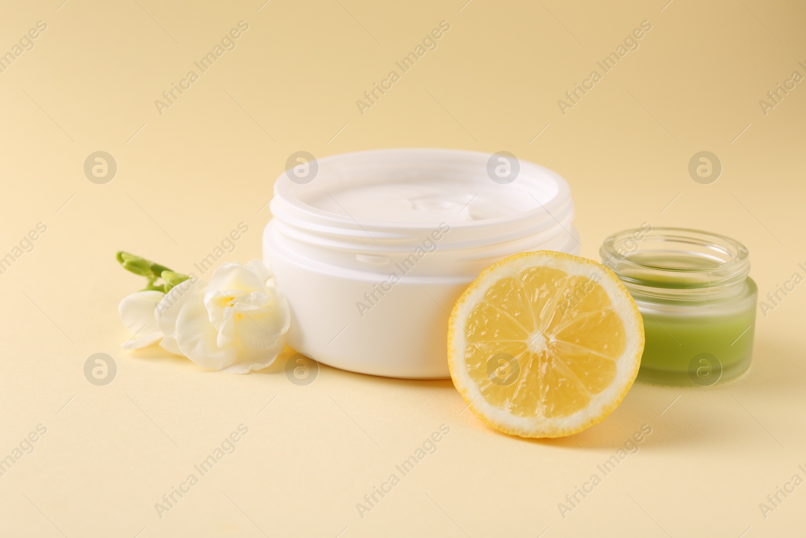 Photo of Moisturizing cream in open jars, lemon and freesia flower on beige background. Body care products