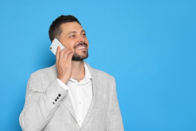 Photo of Handsome man talking on phone against light blue background. Space for text