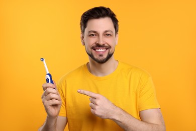 Photo of Happy man holding electric toothbrush on yellow background