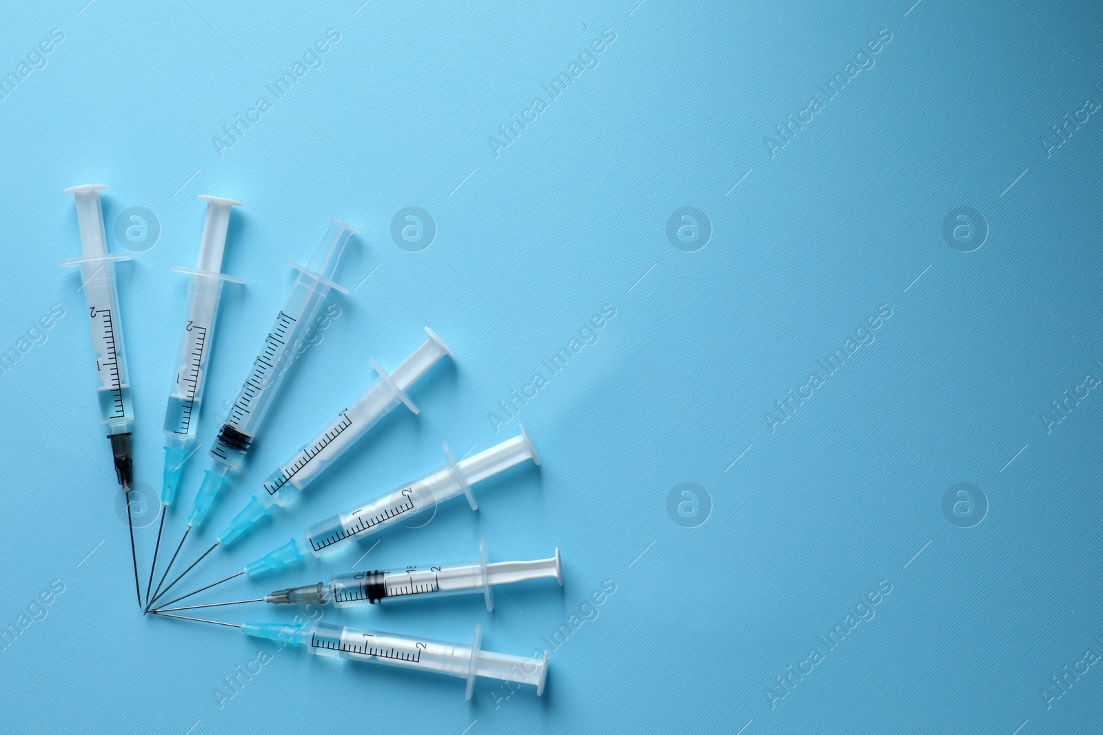 Photo of Disposable syringes with needles and medicine on light blue background, flat lay. Space for text