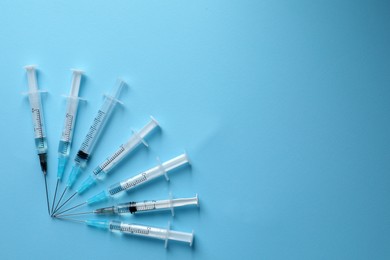Disposable syringes with needles and medicine on light blue background, flat lay. Space for text
