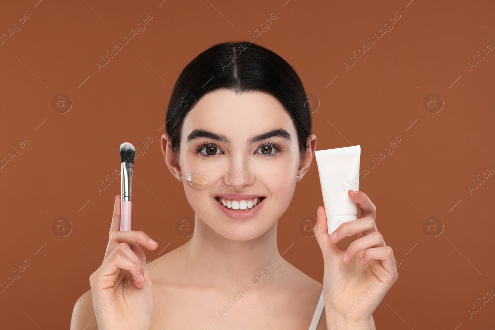 Photo of Teenage girl with tube of foundation and brush on brown background