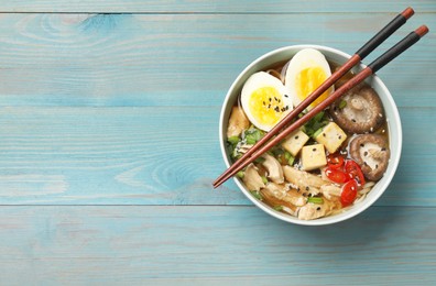 Bowl of delicious ramen and chopsticks on light blue wooden table, top view with space for text. Noodle soup