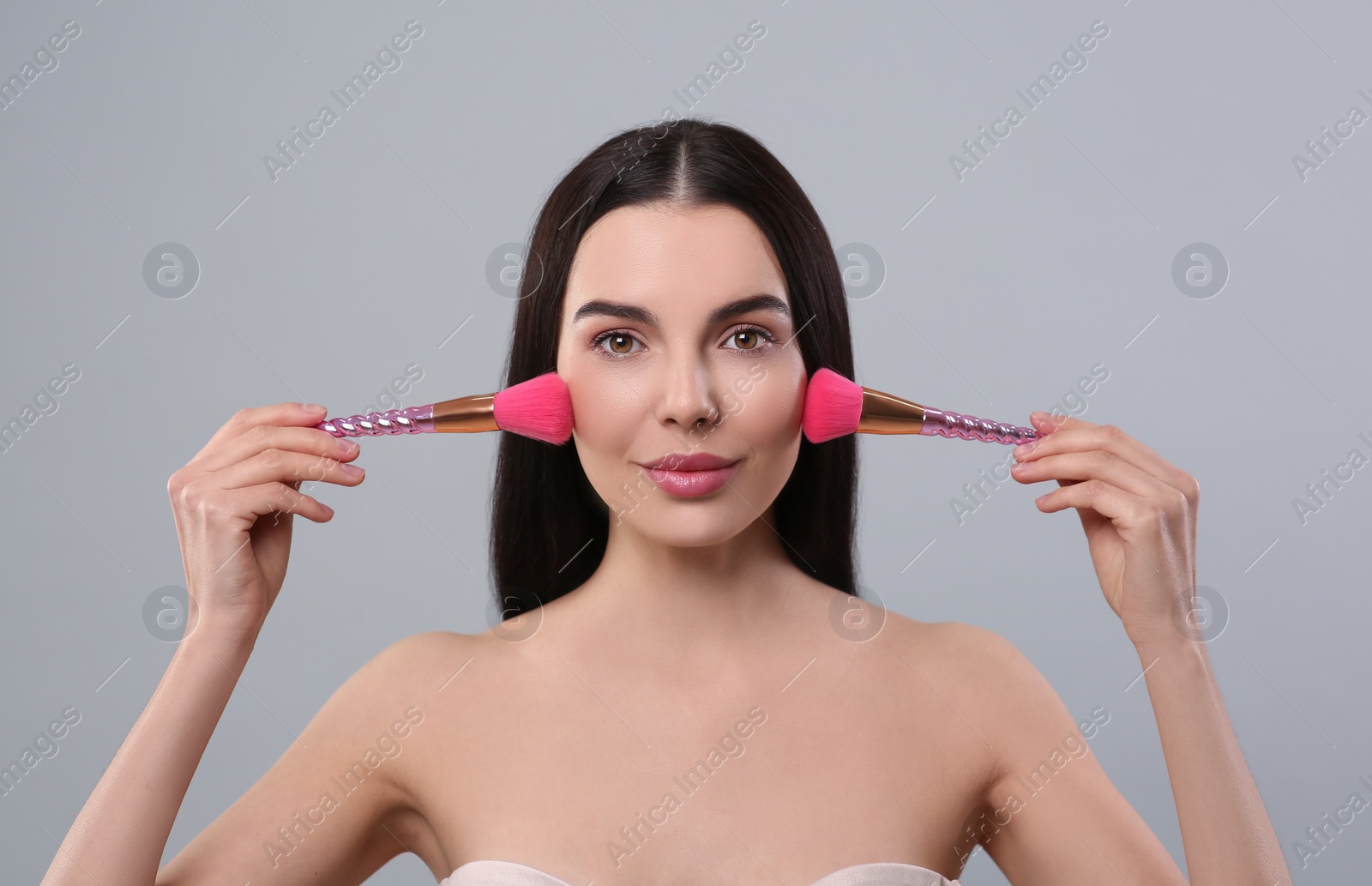 Photo of Beautiful woman with makeup brushes on light grey background