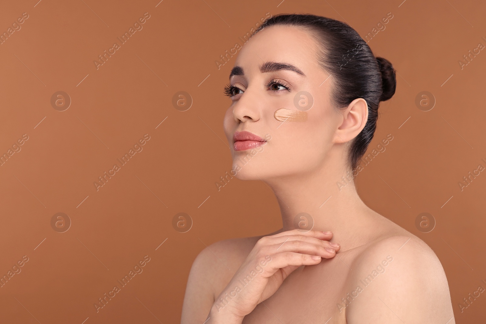 Photo of Woman with swatch of foundation on face against brown background. Space for text