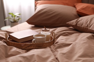 Cup of hot coffee and books on bed with stylish linens in room