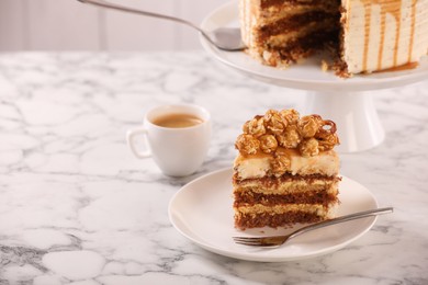 Photo of Piece of caramel drip cake decorated with popcorn and pretzels on white marble table, space for text