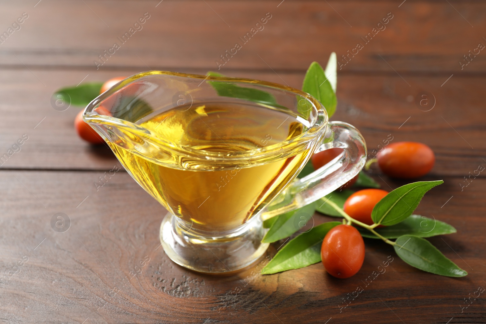 Photo of Glass sauce boat with jojoba oil and seeds on wooden table