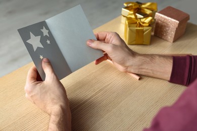 Man holding greeting card at wooden table, closeup