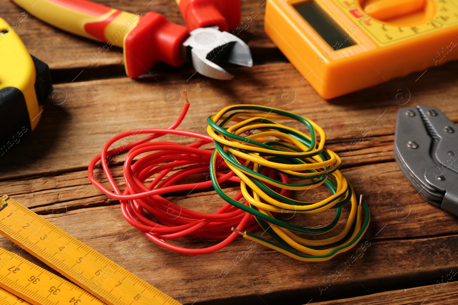 Photo of Wires and electrician's tools on wooden table, closeup