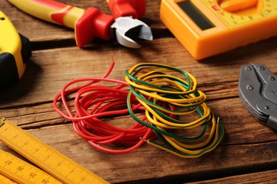 Photo of Wires and electrician's tools on wooden table, closeup