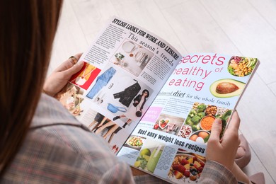 Woman reading cooking magazine indoors, closeup view