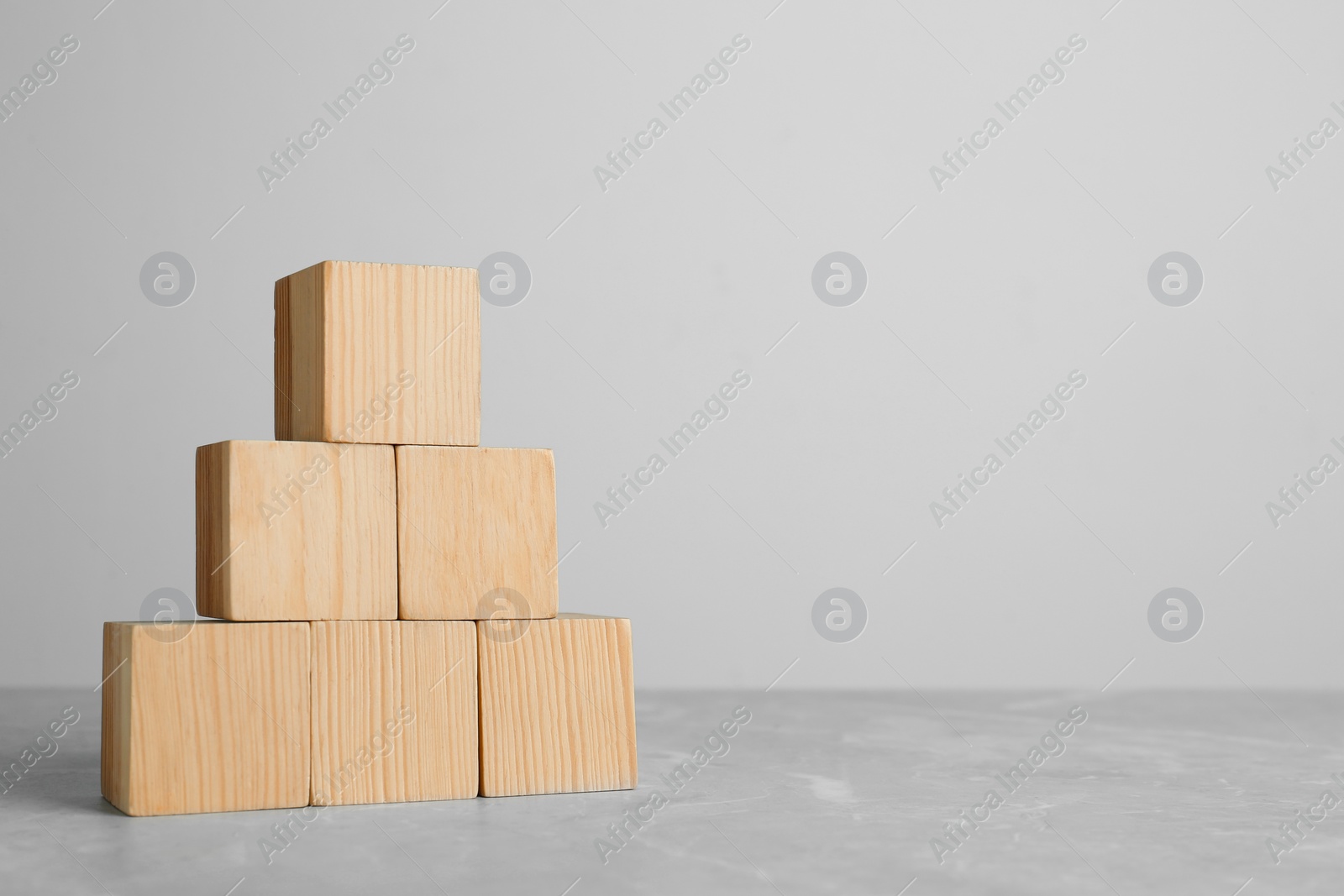 Photo of Pyramid of blank wooden cubes on grey table against light background. Space for text