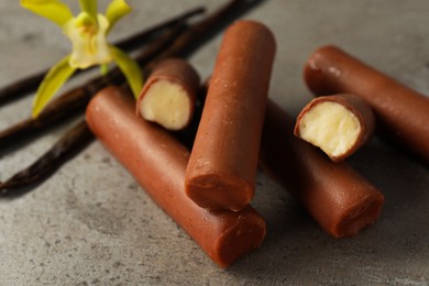 Photo of Glazed curd cheese bars, vanilla pods and flower on grey table, closeup