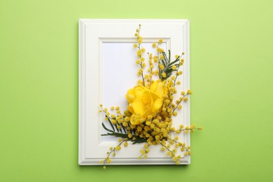 Photo of Beautiful floral composition with mimosa flowers and frame on green background, top view
