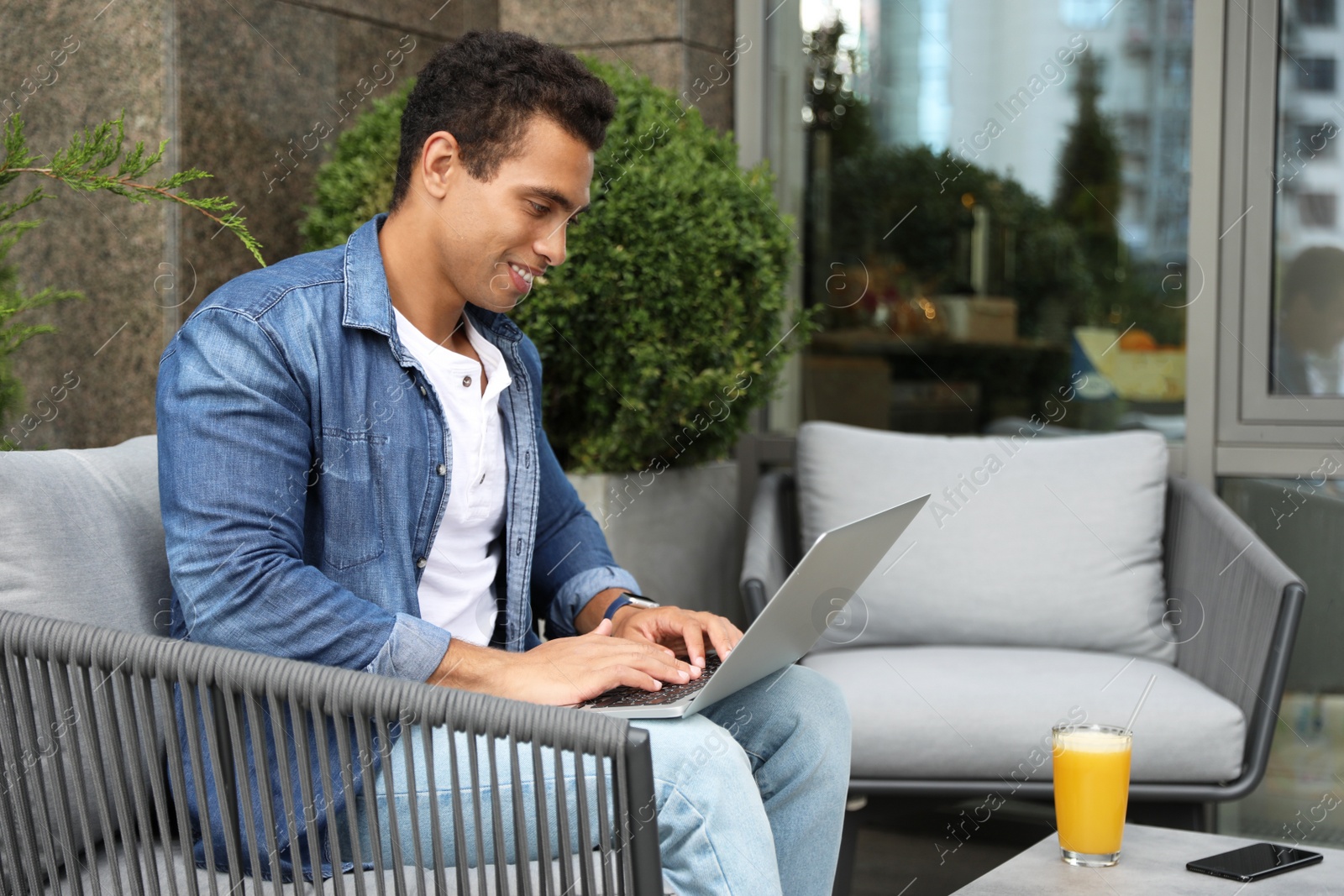 Photo of Portrait of handsome young African-American man with laptop in outdoor cafe