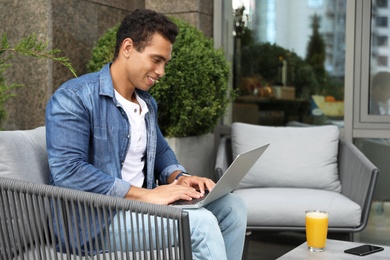 Portrait of handsome young African-American man with laptop in outdoor cafe