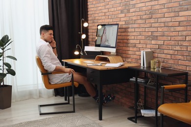 Photo of Businessman in shirt and underwear talking on mobile phone near computer at home office