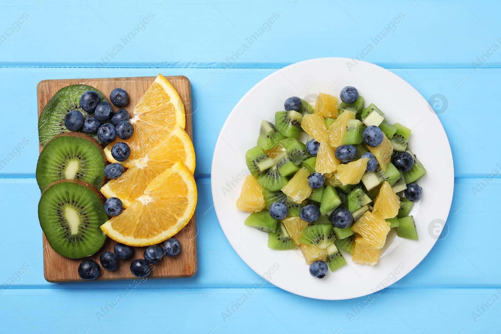 Photo of Plate of tasty fruit salad and ingredients on light blue wooden table, flat lay