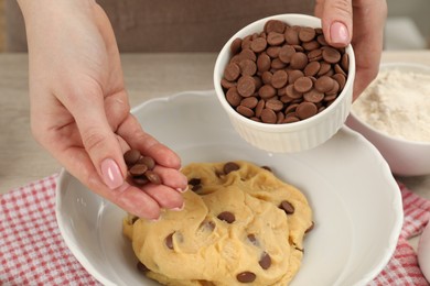 Photo of Cooking sweet cookies. Woman adding chocolate chips to dough at table, closeup