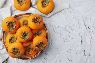 Bowl with delicious ripe juicy persimmons on white textured table, flat lay. Space for text