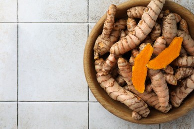 Photo of Bowl with raw turmeric roots on white tiled table, top view. Space for text